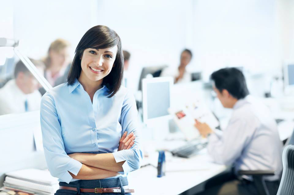 Insurance agent smiling in an office with other agents working 